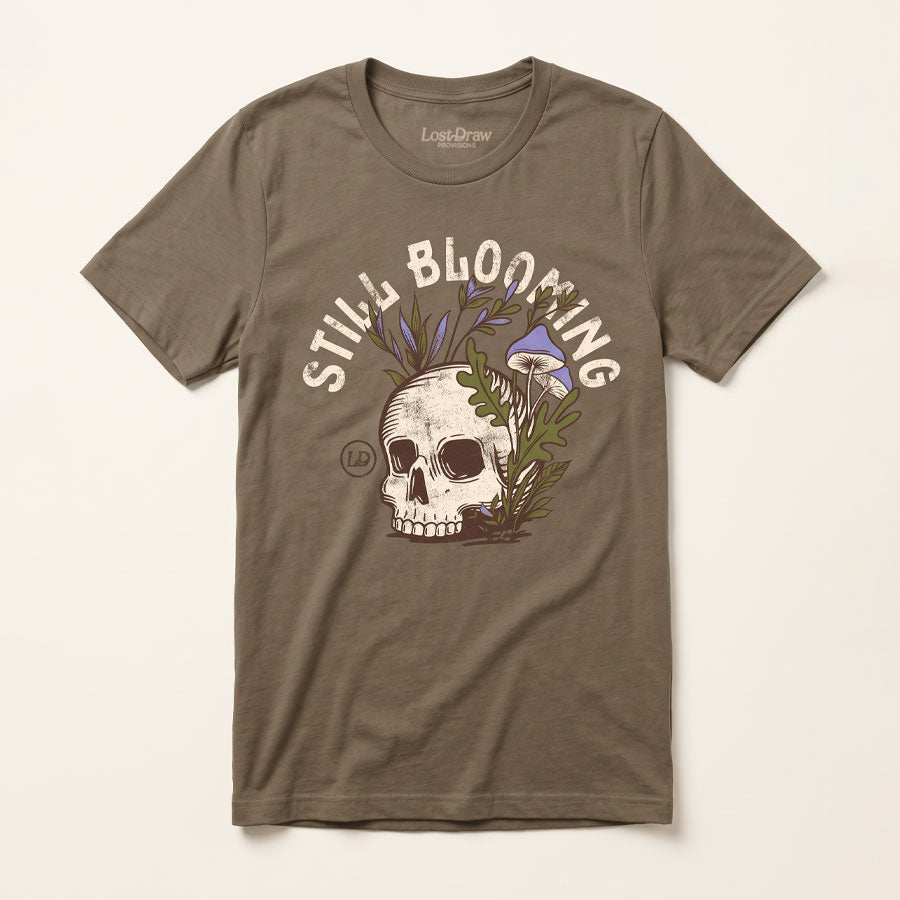 Front of the Still Blooming Jersey Tee in Vintage Brown featuring a vintage skull, lavender mushrooms, and olive green botanical artwork.