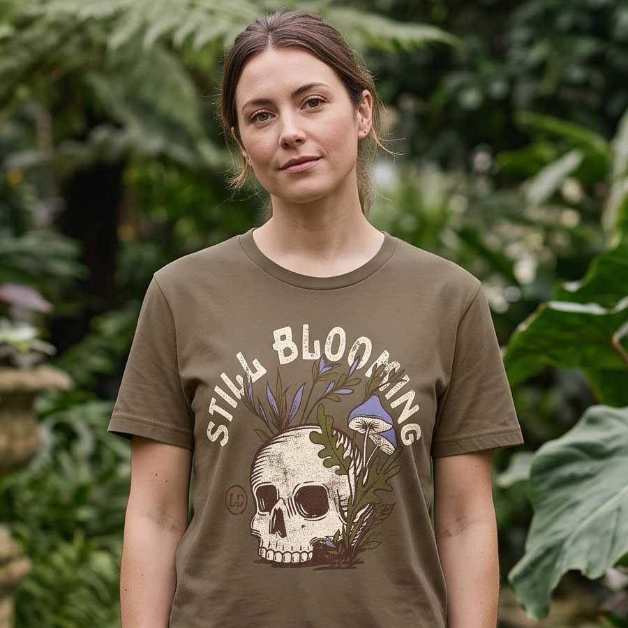 Woman wearing the Vintage Brown Still Blooming Tee in a botanical garden, showing the skull and mushroom graphic.