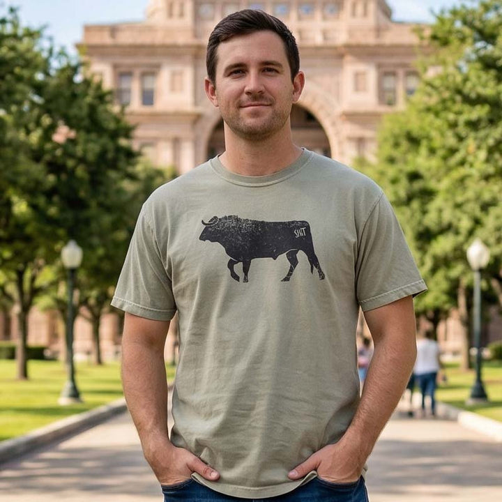 Man wearing a bull shit t-shirt in front of a building with trees