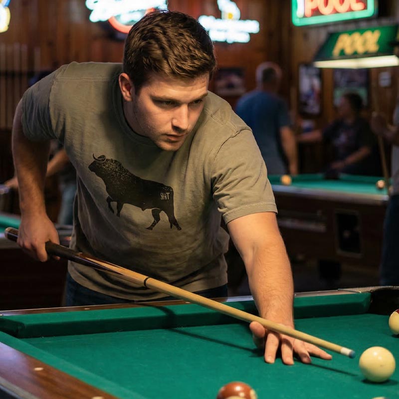 Man playing pool in a bar with neon signs in the background