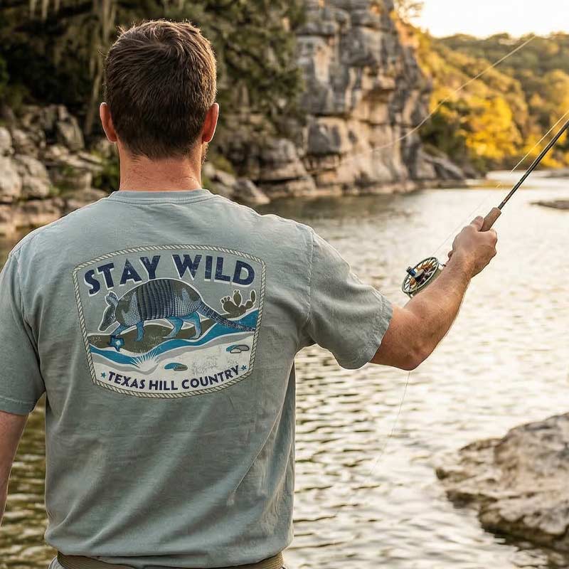 Person wearing Stay Wild Texas Hill Country armadillo t-shirt near a river in the Texas Hill Country
