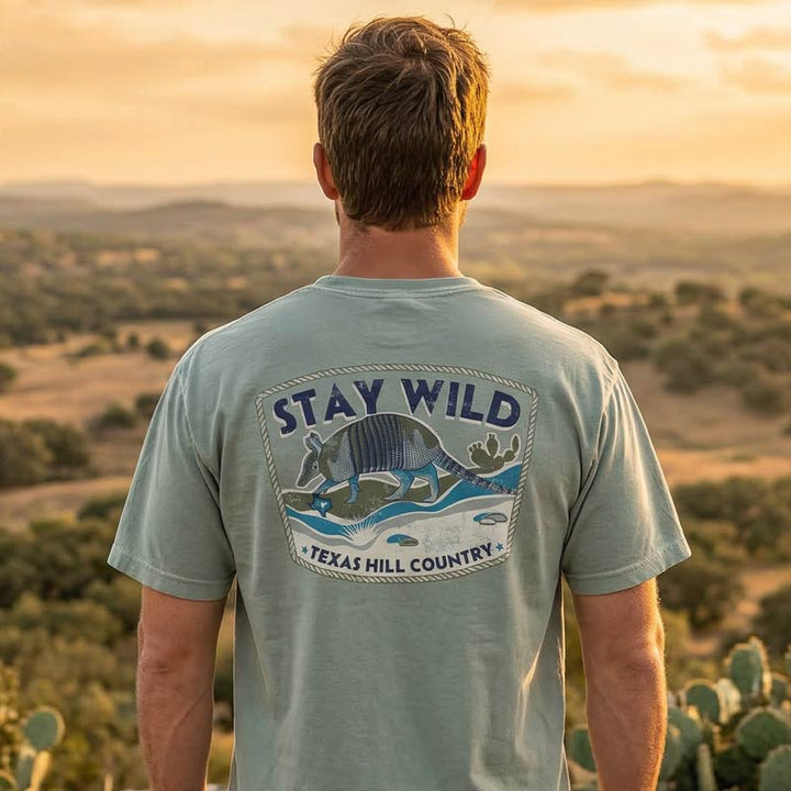 Person wearing Stay Wild Texas Hill Country armadillo t-shirt standing in the Texas Hill Country landscape
