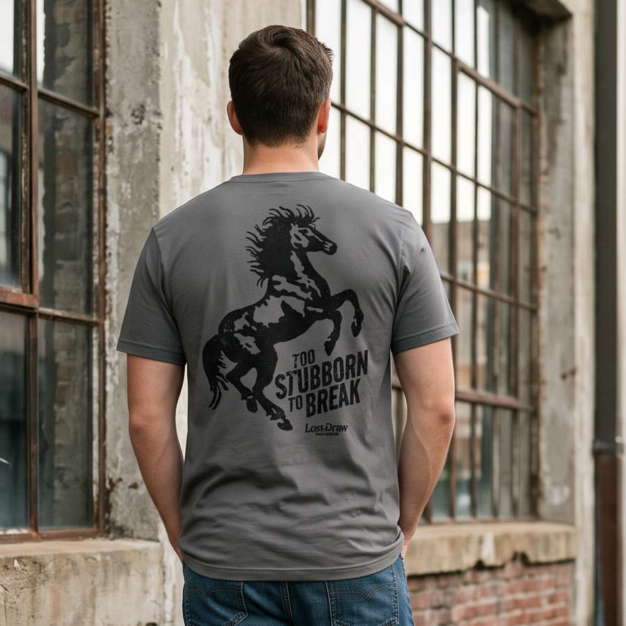 Man wearing the Asphalt Too Stubborn graphic tee outside an industrial warehouse, showing the large rearing horse design.
